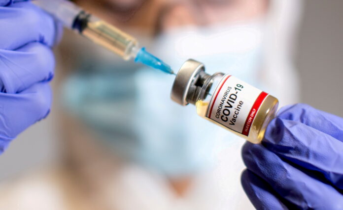 m_FILE PHOTO: A woman holds a medical syringe and a small bottle labelled "Coronavirus COVID-19 Vaccine